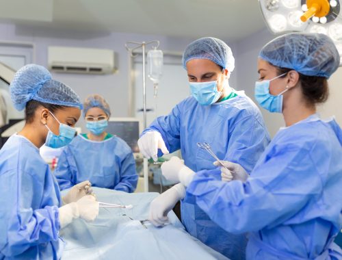 Diverse Team of Professional surgeon, Assistants and Nurses Performing Invasive Surgery on a Patient in the Hospital Operating Room. Surgeons Talk and Use Instruments. Real Modern Hospital.