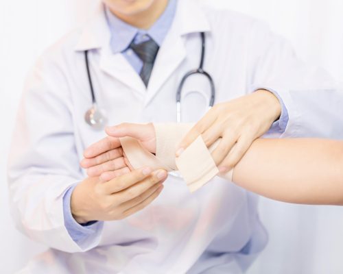 Male doctor putting gauze on young man's hand in clinic, closeup. First aid